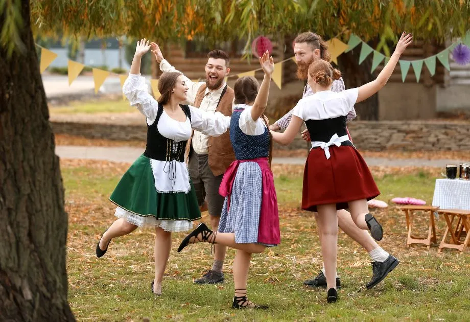 Traditional Bavarian Oktoberfest clothing: women in dirndl with apron, men are in brown lederhosen with checkered shirt, dancing together to celebrate the festival