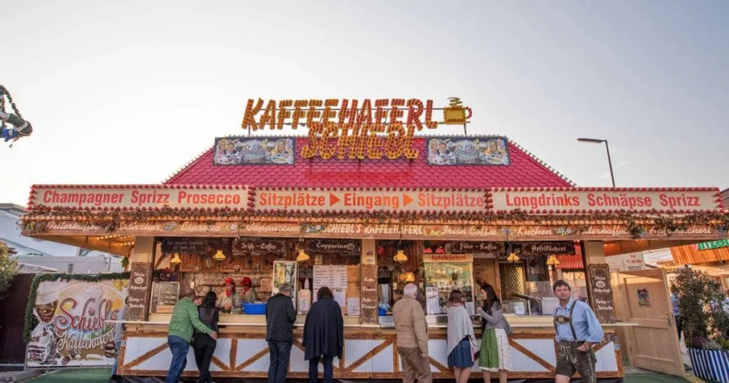 Vintage café sign for Schiebl's-Kaffeehaferl at Oktoberfest, advertising champagne, prosecco, and long drinks with 'Kapperhamerl' header and 'Sitzplatze' (seating) labels in rustic typography.